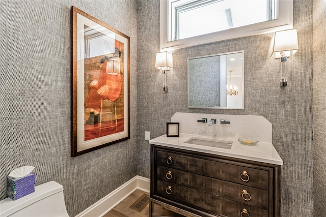 half bath with toilet, vanity, visible vents, and baseboards