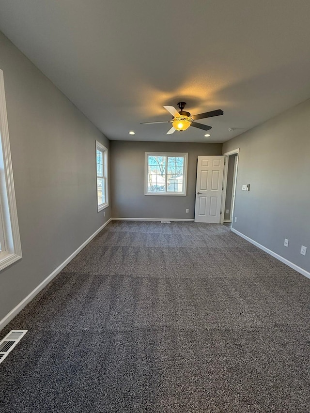 spare room featuring ceiling fan, visible vents, baseboards, and dark colored carpet