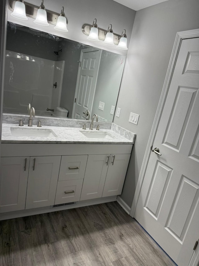 full bath with double vanity, wood finished floors, a sink, and toilet