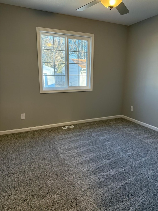 spare room featuring ceiling fan, visible vents, dark colored carpet, and baseboards