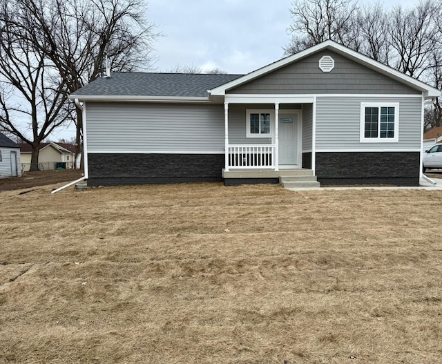 view of front of house with stone siding, a porch, a front lawn, and roof with shingles