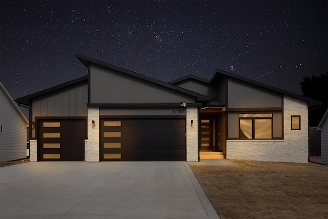 contemporary home featuring stone siding, board and batten siding, and concrete driveway