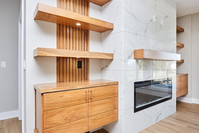 interior space with baseboards, open shelves, a glass covered fireplace, and light wood-style floors