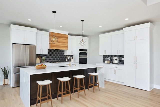 kitchen featuring stainless steel appliances, light wood finished floors, backsplash, and a center island with sink