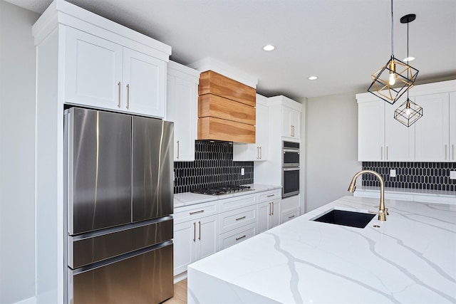 kitchen with appliances with stainless steel finishes, a sink, premium range hood, white cabinetry, and backsplash