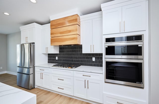 kitchen with stainless steel appliances, white cabinets, light wood finished floors, light stone countertops, and tasteful backsplash