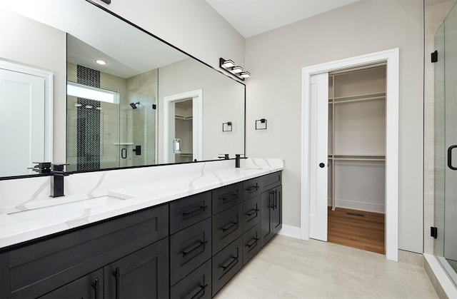 bathroom featuring double vanity, a stall shower, a walk in closet, and a sink