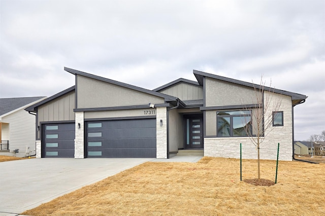 modern home with a garage, stone siding, driveway, and board and batten siding