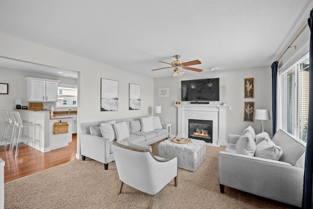 living area featuring a glass covered fireplace, plenty of natural light, a textured ceiling, and ceiling fan