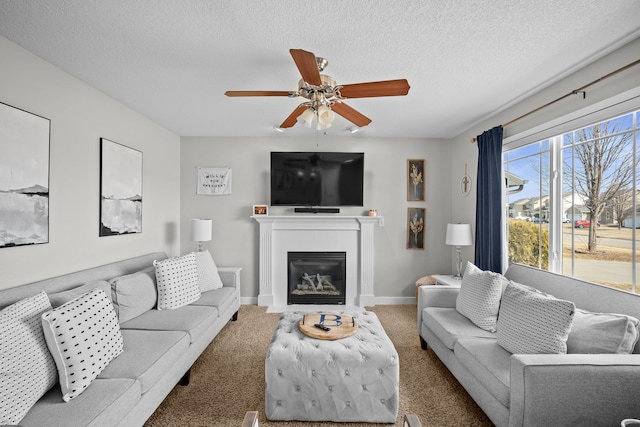 living area with carpet flooring, a textured ceiling, baseboards, and a glass covered fireplace