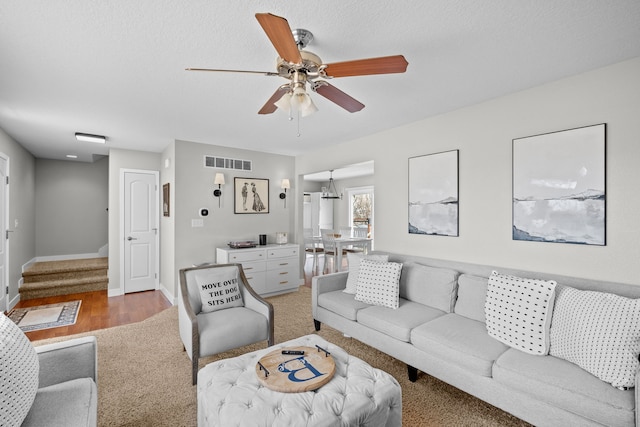 living room featuring visible vents, baseboards, stairway, light wood-type flooring, and a ceiling fan