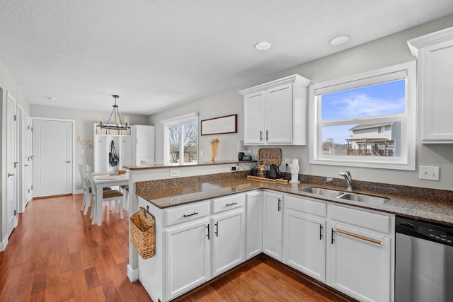 kitchen with a sink, stainless steel dishwasher, wood finished floors, white cabinetry, and a peninsula