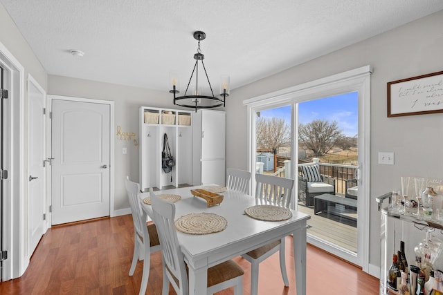 dining area with baseboards, a notable chandelier, wood finished floors, and a textured ceiling