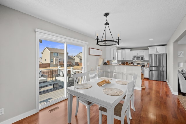 dining area with a textured ceiling, wood finished floors, visible vents, and baseboards