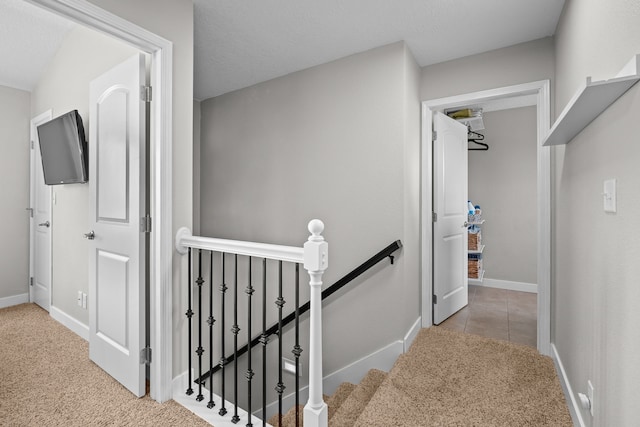 hallway featuring tile patterned flooring, an upstairs landing, baseboards, and carpet floors