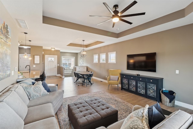 living area with a ceiling fan, baseboards, a raised ceiling, and wood finished floors