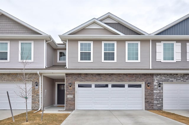 townhome / multi-family property featuring a garage, stone siding, and driveway