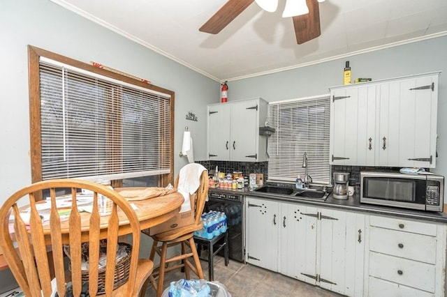 kitchen with dishwasher, dark countertops, stainless steel microwave, crown molding, and a sink