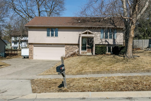 bi-level home featuring driveway, an attached garage, fence, and brick siding