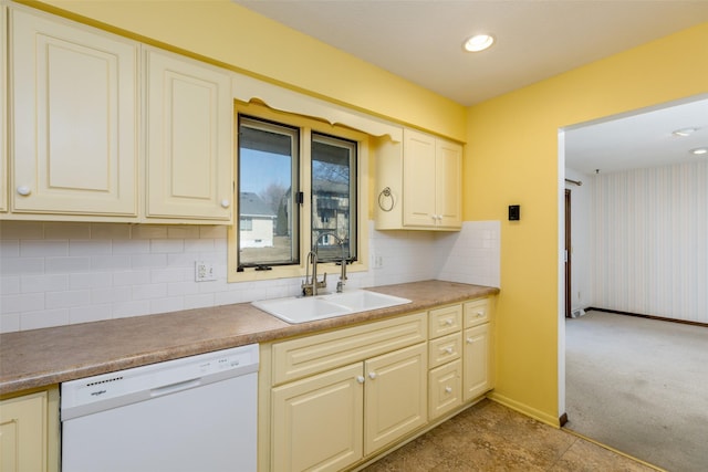 kitchen featuring backsplash, light carpet, white dishwasher, a sink, and baseboards