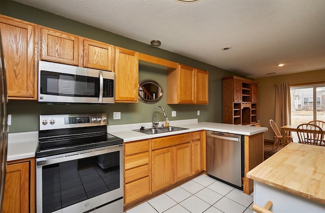 kitchen featuring butcher block countertops, a peninsula, stainless steel appliances, a sink, and recessed lighting