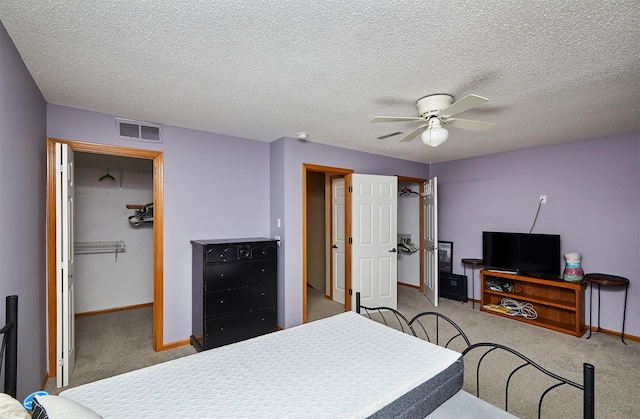 carpeted bedroom with a closet, visible vents, a ceiling fan, a textured ceiling, and baseboards