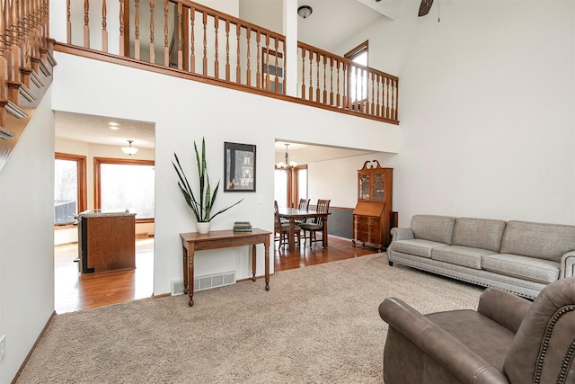 living room featuring visible vents, ceiling fan with notable chandelier, carpet, and a towering ceiling