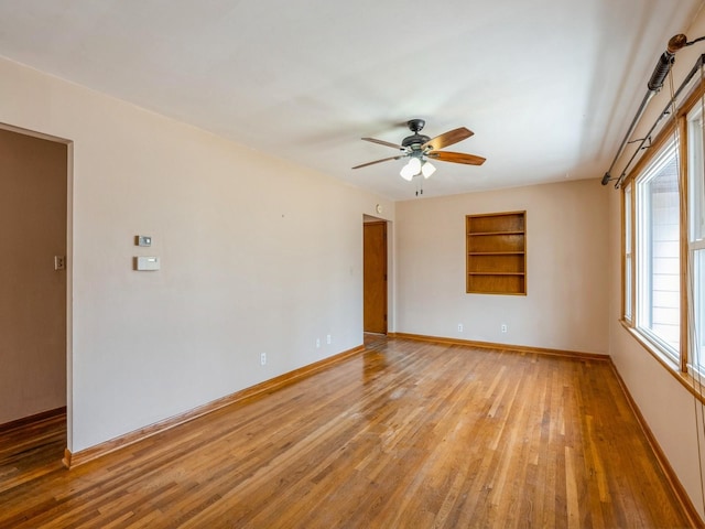 spare room with ceiling fan, light wood-type flooring, built in features, and baseboards