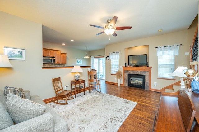 living area with ceiling fan, dark wood-type flooring, a tiled fireplace, and baseboards