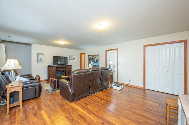 living room with a glass covered fireplace, wood finished floors, and baseboards