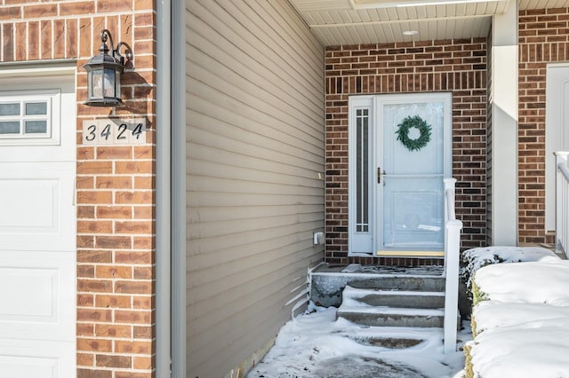 snow covered property entrance with a garage and brick siding