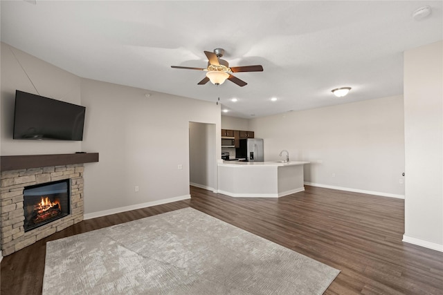 unfurnished living room featuring ceiling fan, dark wood-type flooring, a fireplace, and baseboards