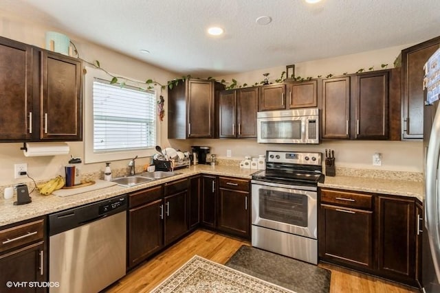 kitchen with dark brown cabinetry, light wood-style flooring, stainless steel appliances, a textured ceiling, and a sink