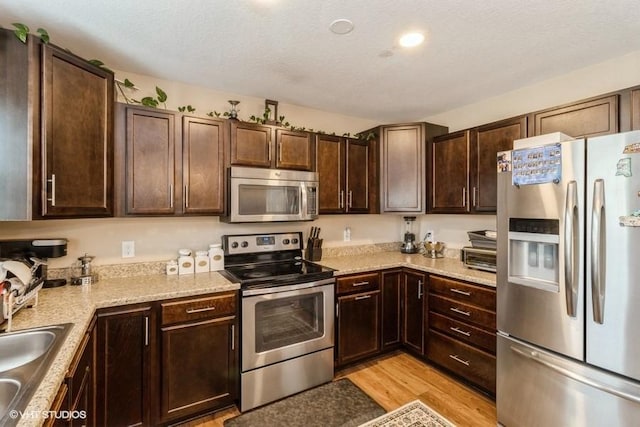 kitchen with a textured ceiling, a sink, dark brown cabinets, appliances with stainless steel finishes, and light wood finished floors