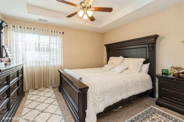 bedroom with visible vents, a tray ceiling, a ceiling fan, and light colored carpet