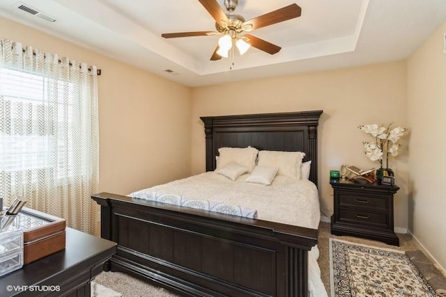 bedroom featuring a tray ceiling, visible vents, ceiling fan, and baseboards