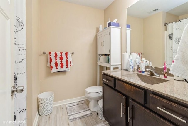 full bath with visible vents, toilet, vanity, wood finished floors, and baseboards