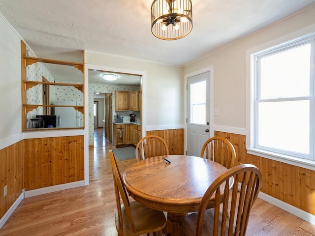 dining room featuring crown molding, light wood finished floors, wainscoting, wood walls, and a chandelier