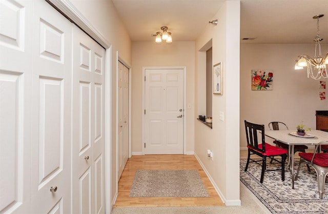 doorway with light wood finished floors, baseboards, and a notable chandelier