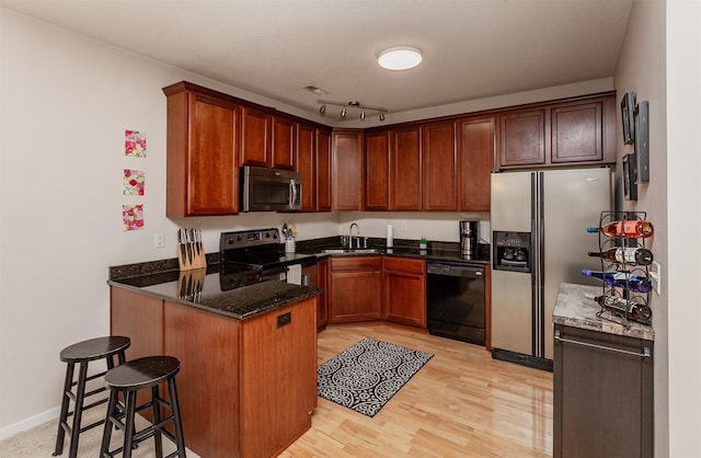 kitchen featuring light wood-style flooring, stainless steel appliances, a peninsula, a sink, and dark stone counters