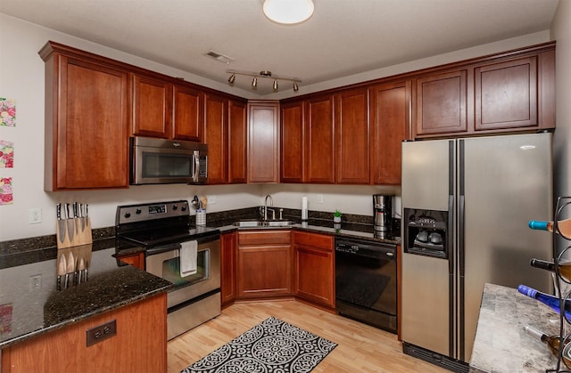 kitchen with visible vents, light wood-style flooring, appliances with stainless steel finishes, a sink, and dark stone countertops