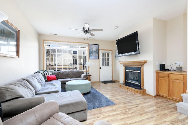 living room featuring visible vents, a ceiling fan, a glass covered fireplace, light wood-type flooring, and baseboards