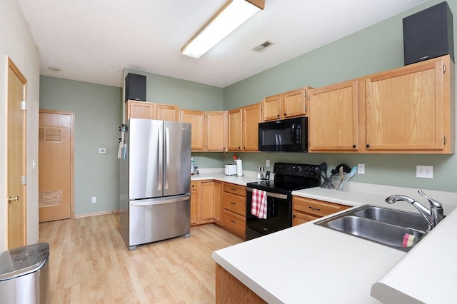 kitchen with a sink, visible vents, light brown cabinetry, light wood-type flooring, and black appliances