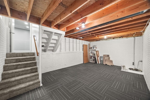 unfinished basement with brick wall, stairs, and dark carpet