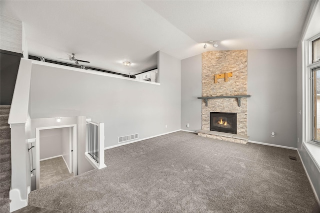 unfurnished living room featuring visible vents, lofted ceiling, stairs, a stone fireplace, and carpet floors