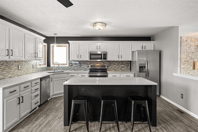 kitchen featuring stainless steel appliances, a sink, white cabinetry, a center island, and a kitchen bar