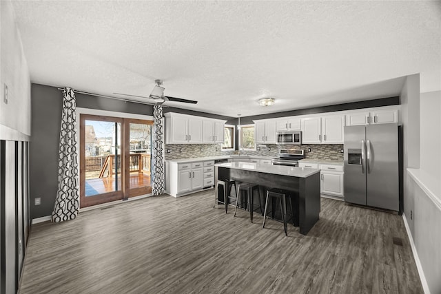 kitchen with dark wood-style floors, a center island, stainless steel appliances, light countertops, and white cabinetry