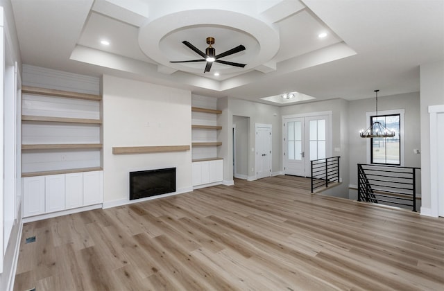 unfurnished living room with light wood-style flooring, recessed lighting, ceiling fan with notable chandelier, a fireplace, and a tray ceiling