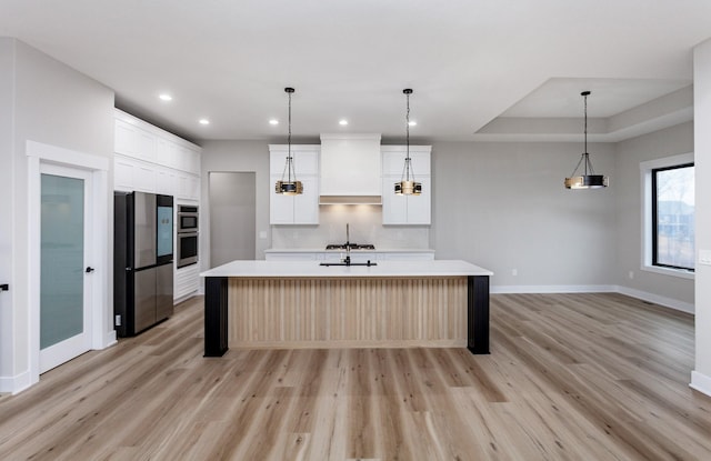 kitchen with light wood-style floors, a kitchen island with sink, light countertops, and freestanding refrigerator