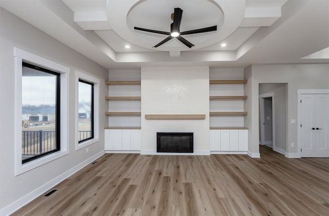 unfurnished living room with a tray ceiling, a glass covered fireplace, light wood-style flooring, and baseboards